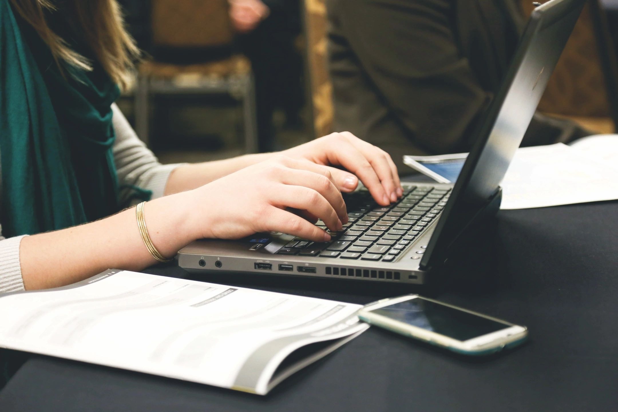Person typing on a laptop with notes and phone nearby